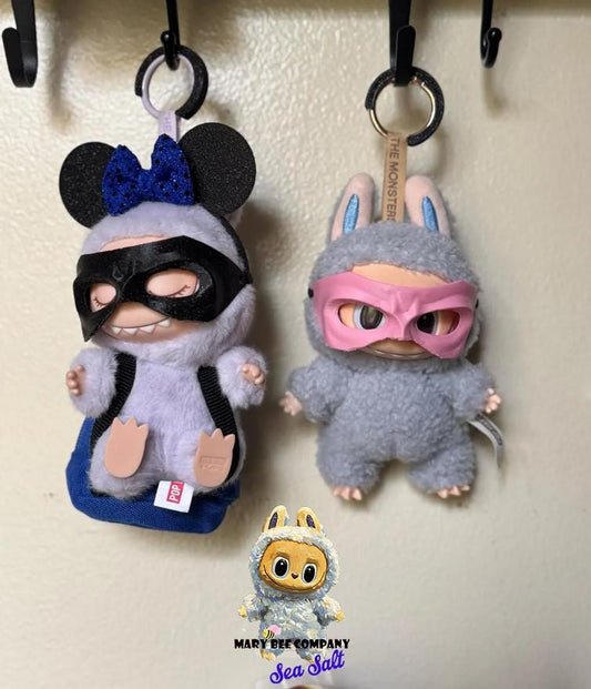 Adorable Labubu dolls in superhero costumes, one with black mask and mouse ears, the other in a bunny suit, perfect for collectors.