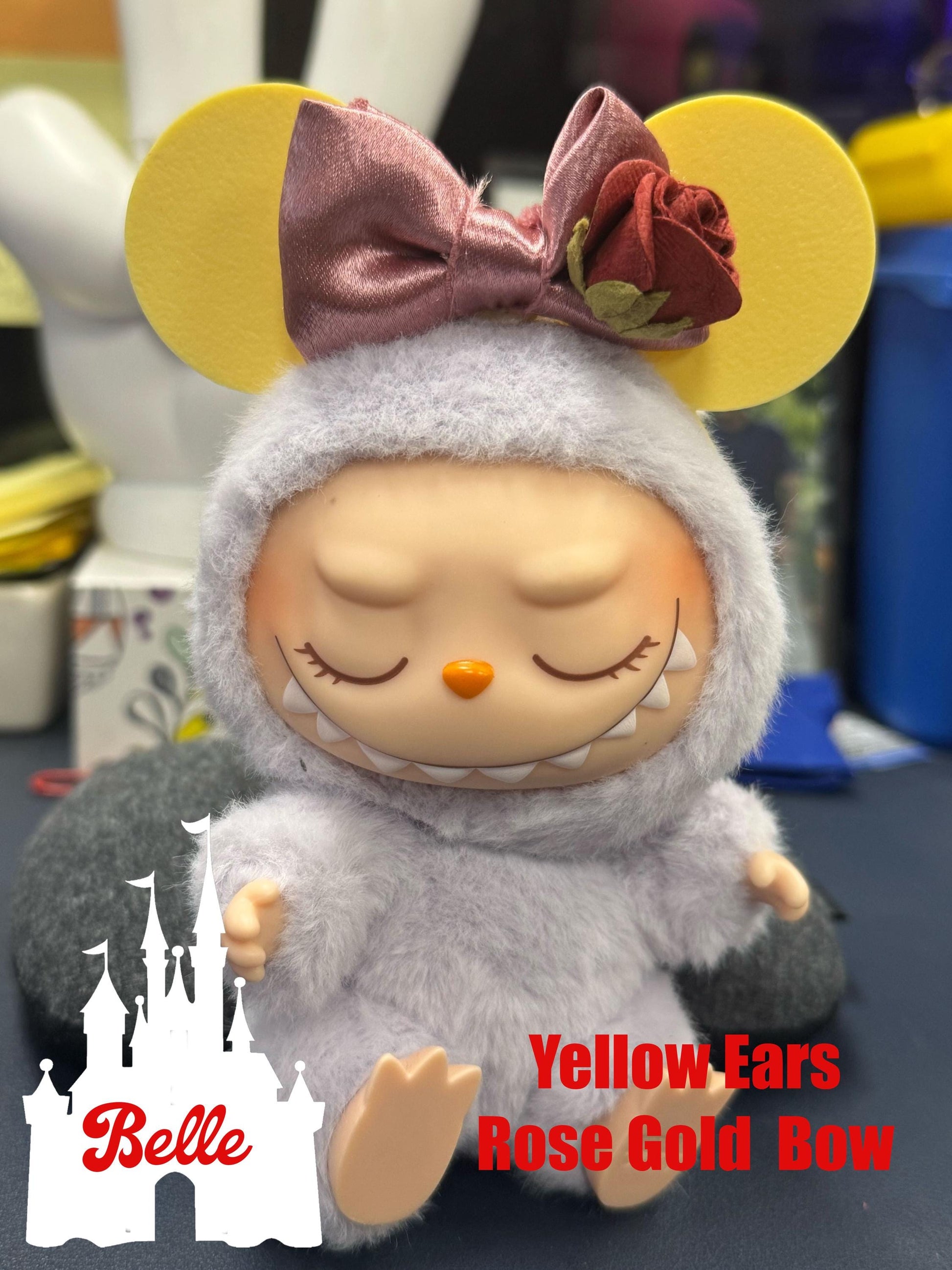 Adorable Labubu doll with yellow ears, rose gold bow, and fuzzy outfit, perfect for collectors and Disney fans.
